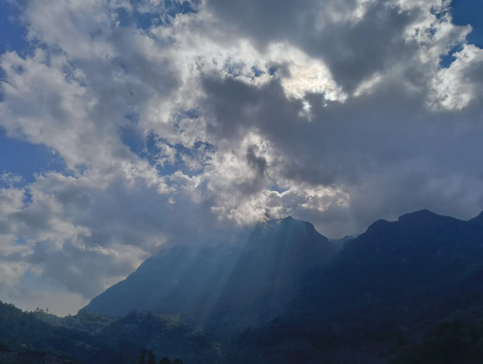 Sun rays breaking through heavy clouds over a dark mountain ridge