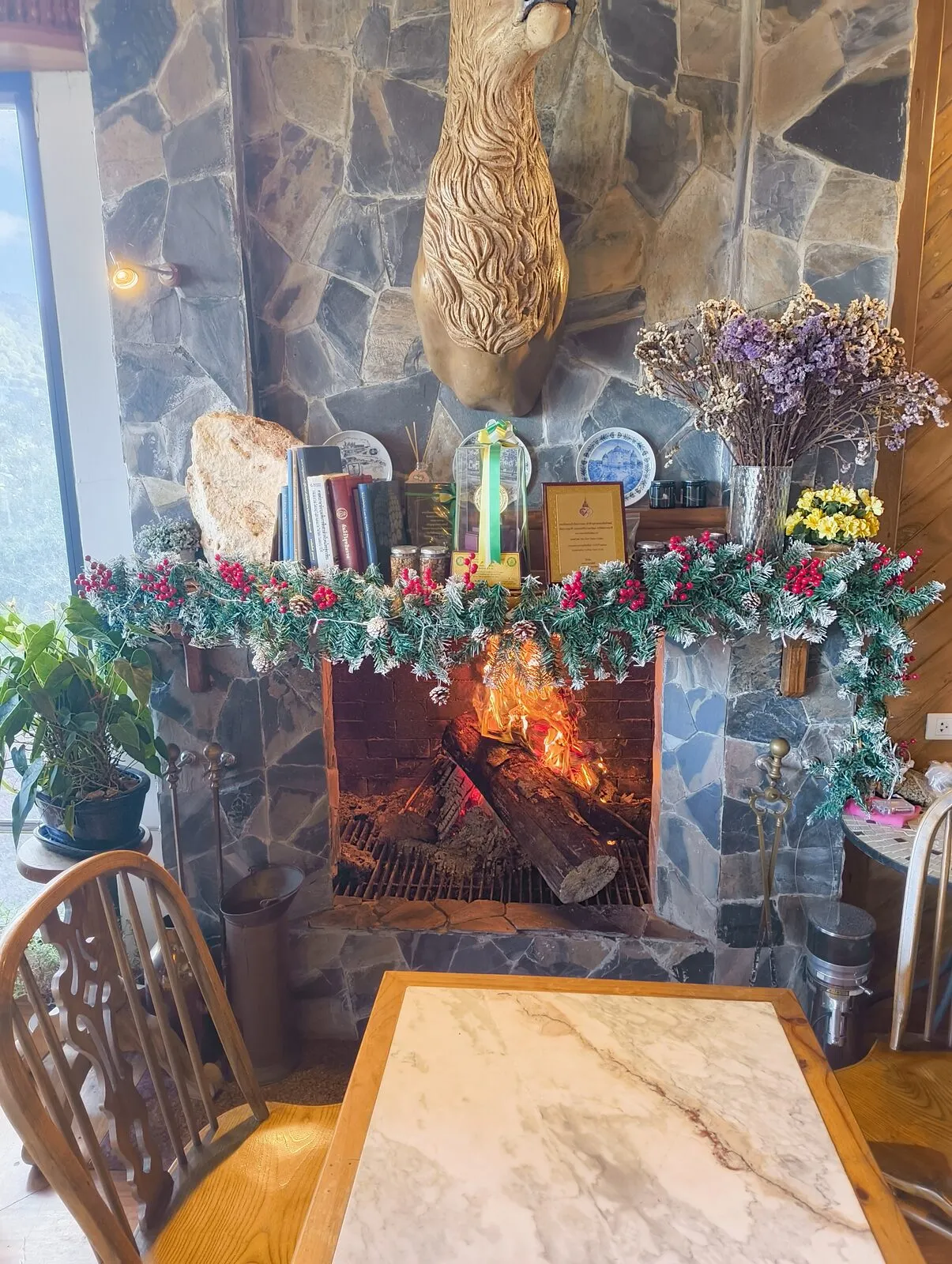 A stone fireplace decorated with Christmas garlands beneath a mounted deer head