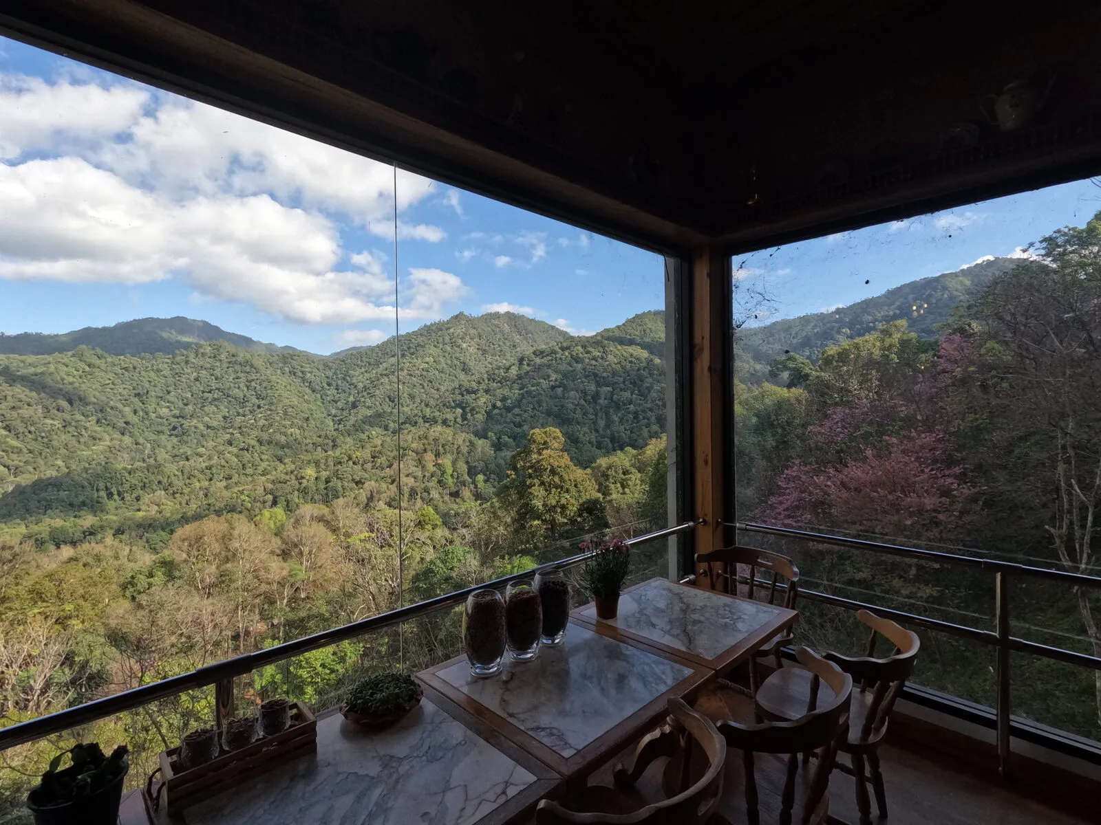 A wooden table and chairs beside a window framing green mountains