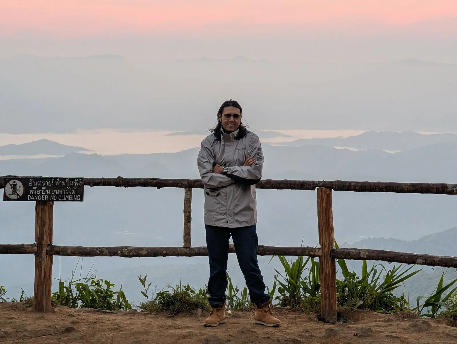 A traveller standing by a wooden sign above a valley filled with mist
