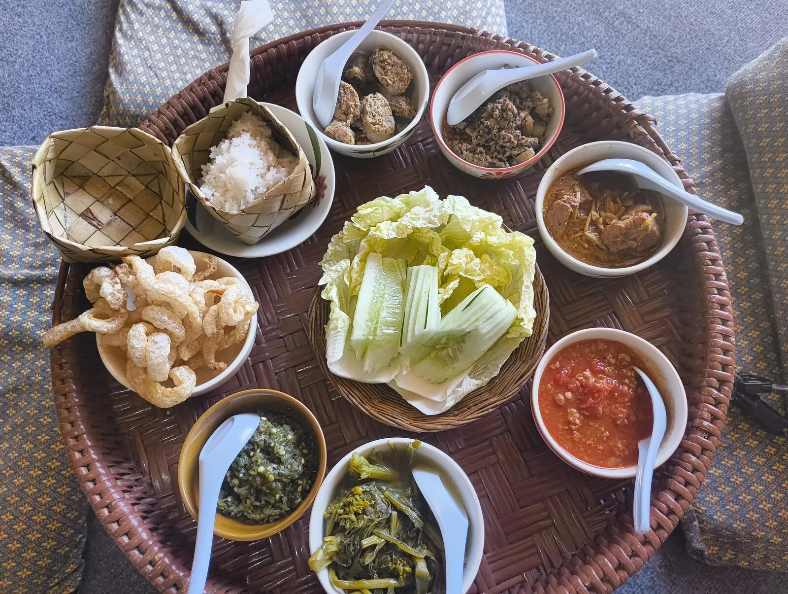 A woven tray of northern Thai dishes with noodles, vegetables and dipping sauces