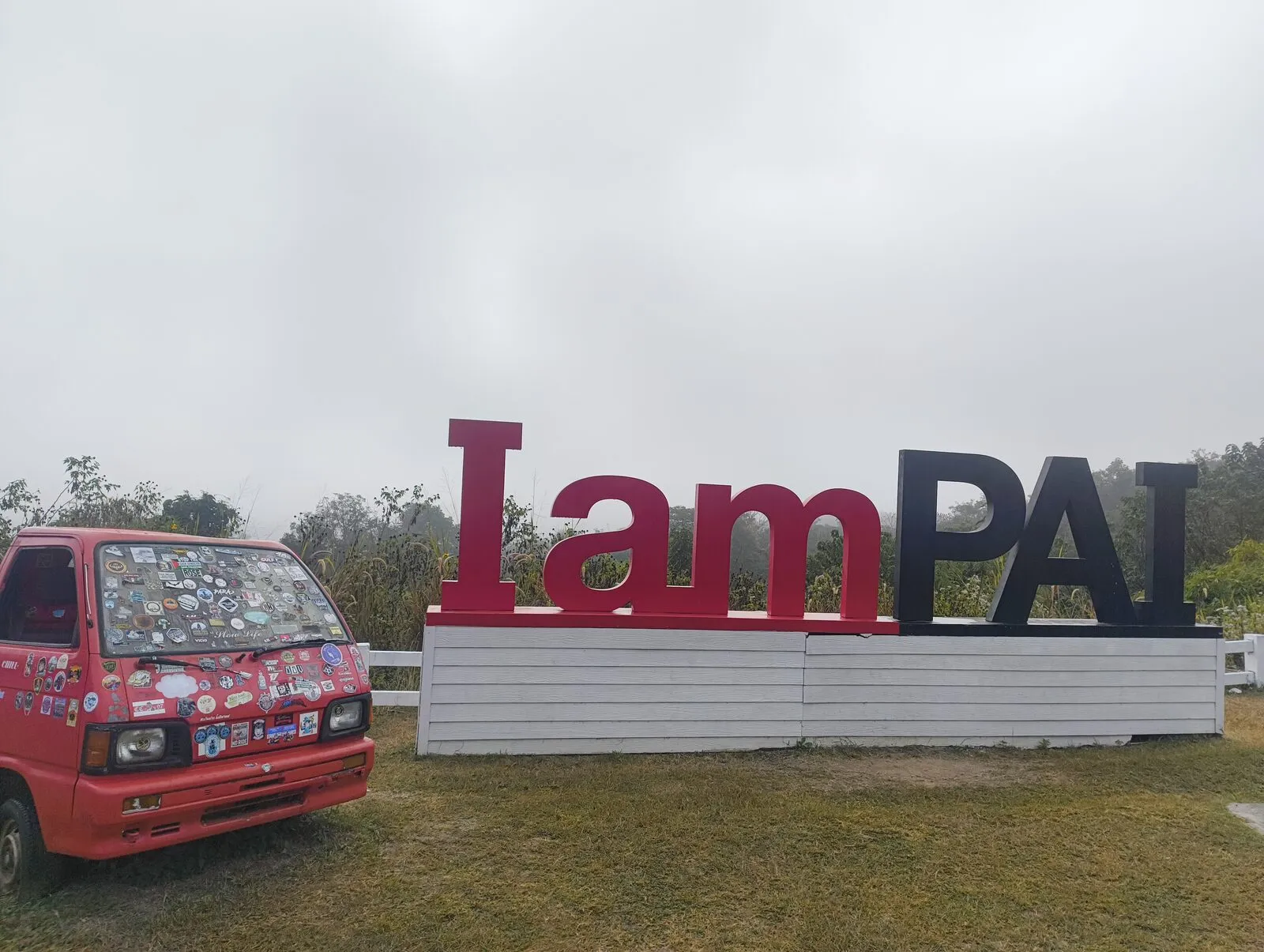 A red songthaew parked beside a large Lam Pai sign