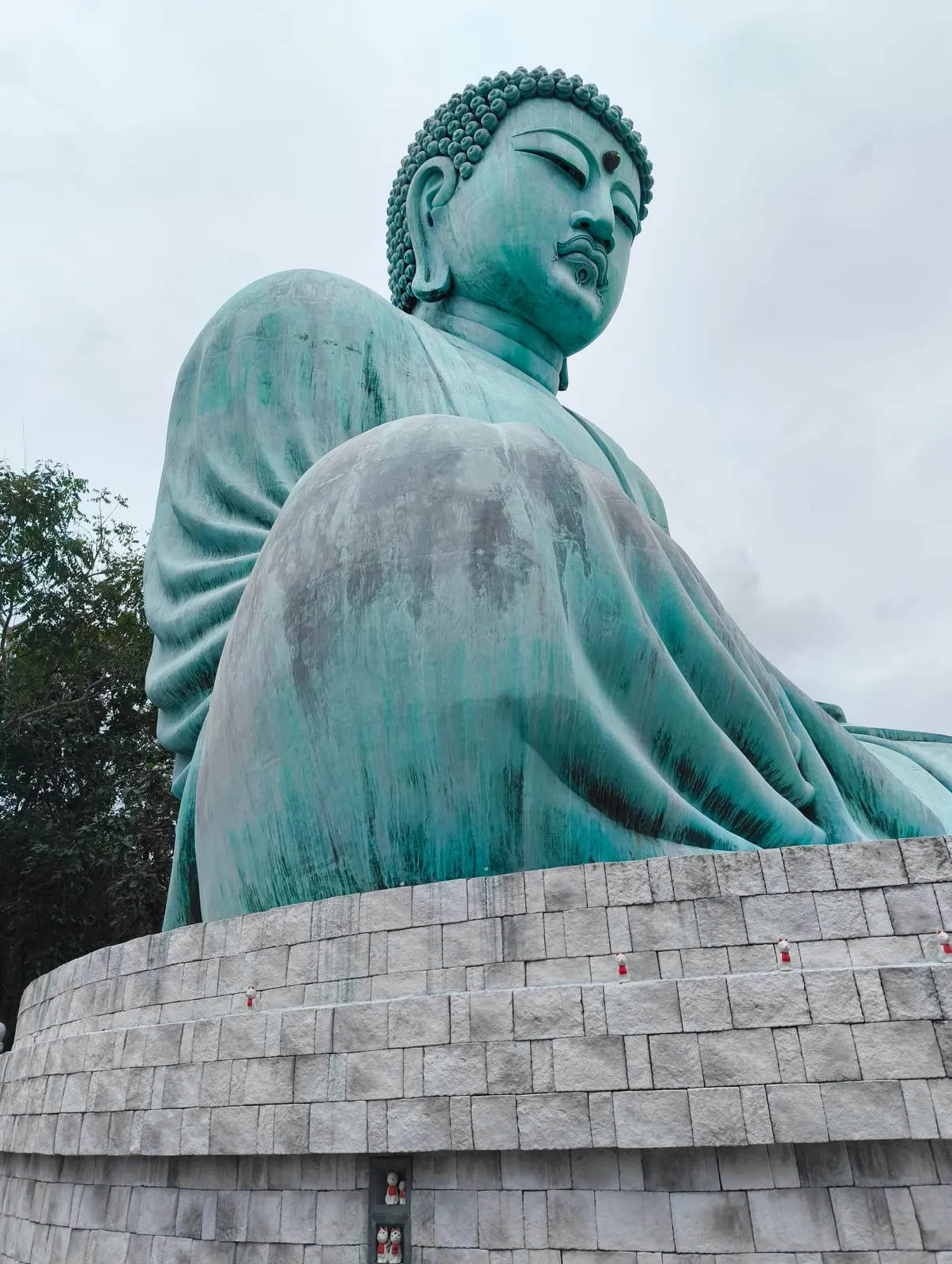 A low angle up the teal Buddha's shoulder and face above a stone base