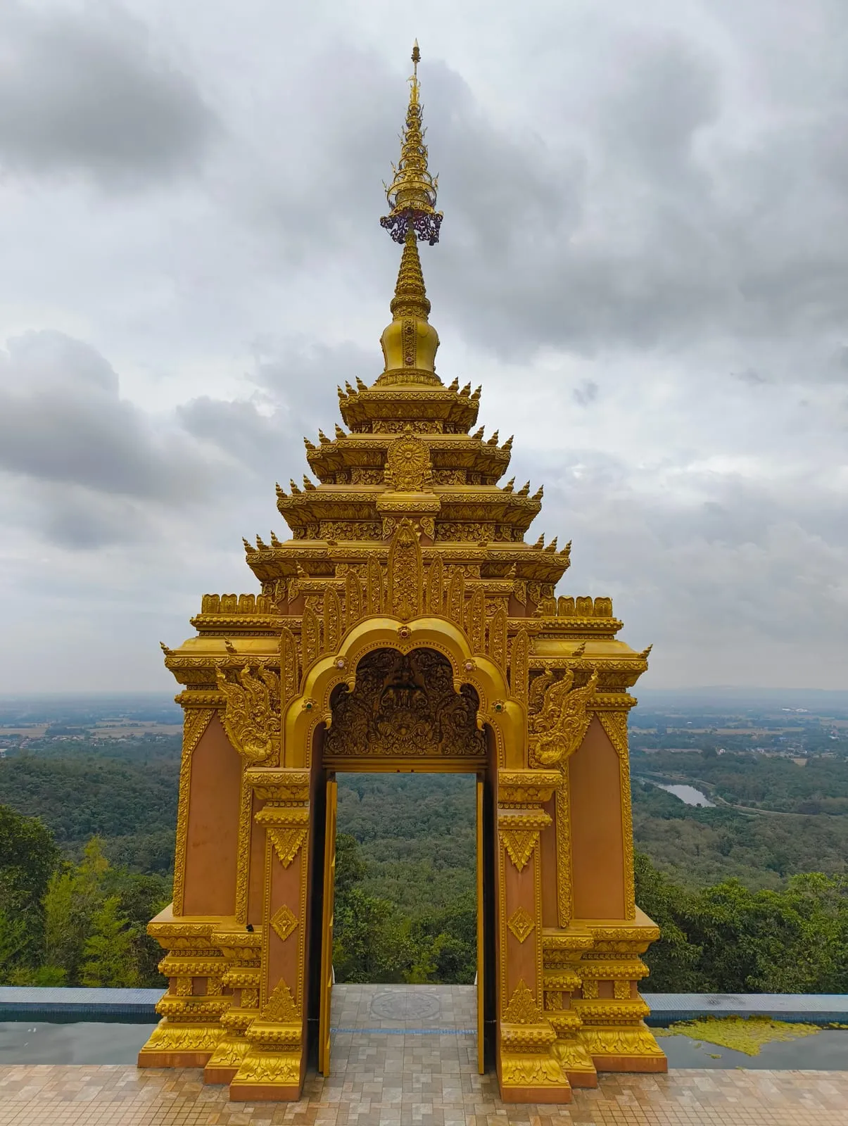 An ornate golden gate opening onto a green valley under heavy cloud