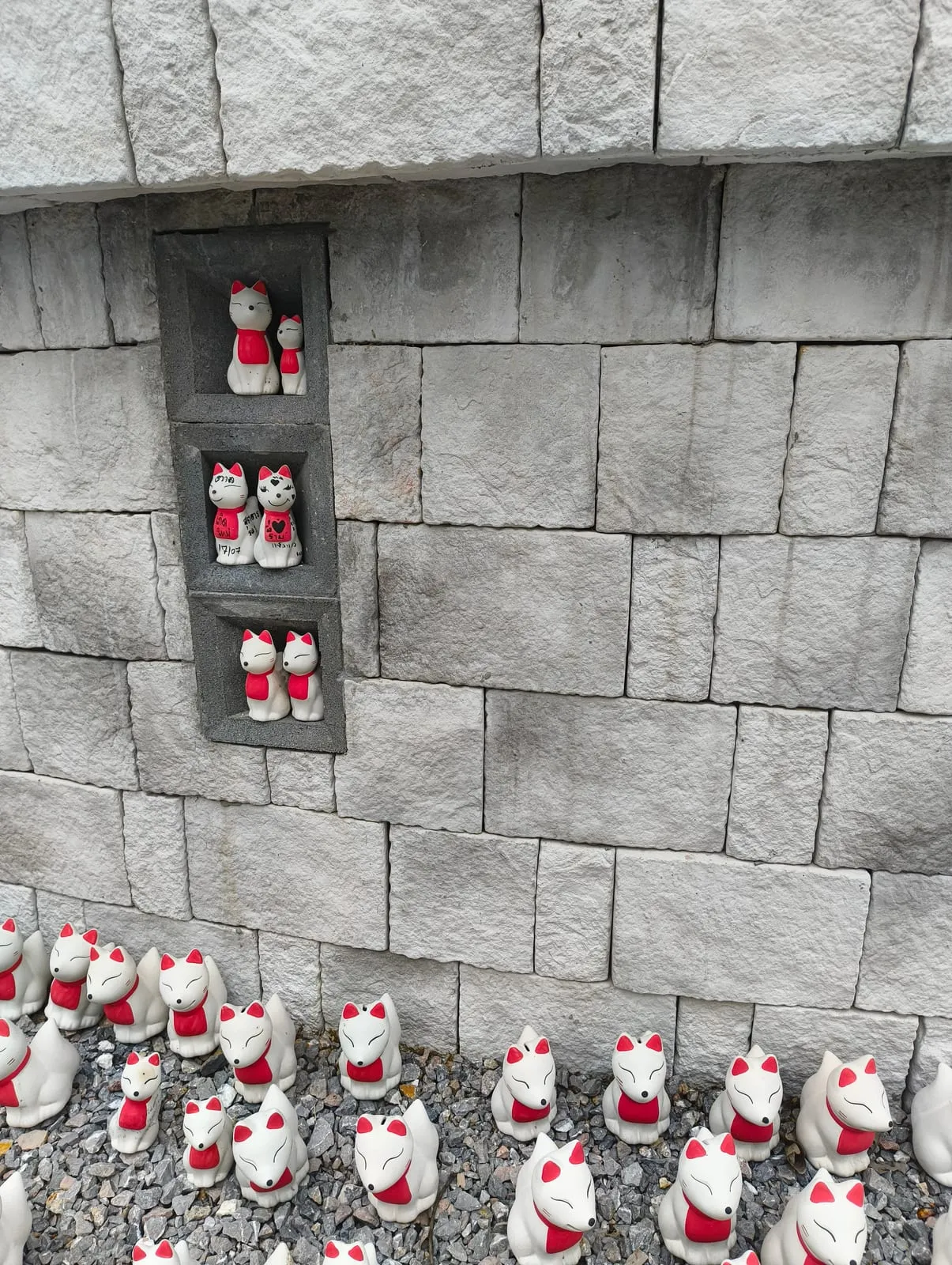 White fox statues with red bibs set into stone niches and on gravel below
