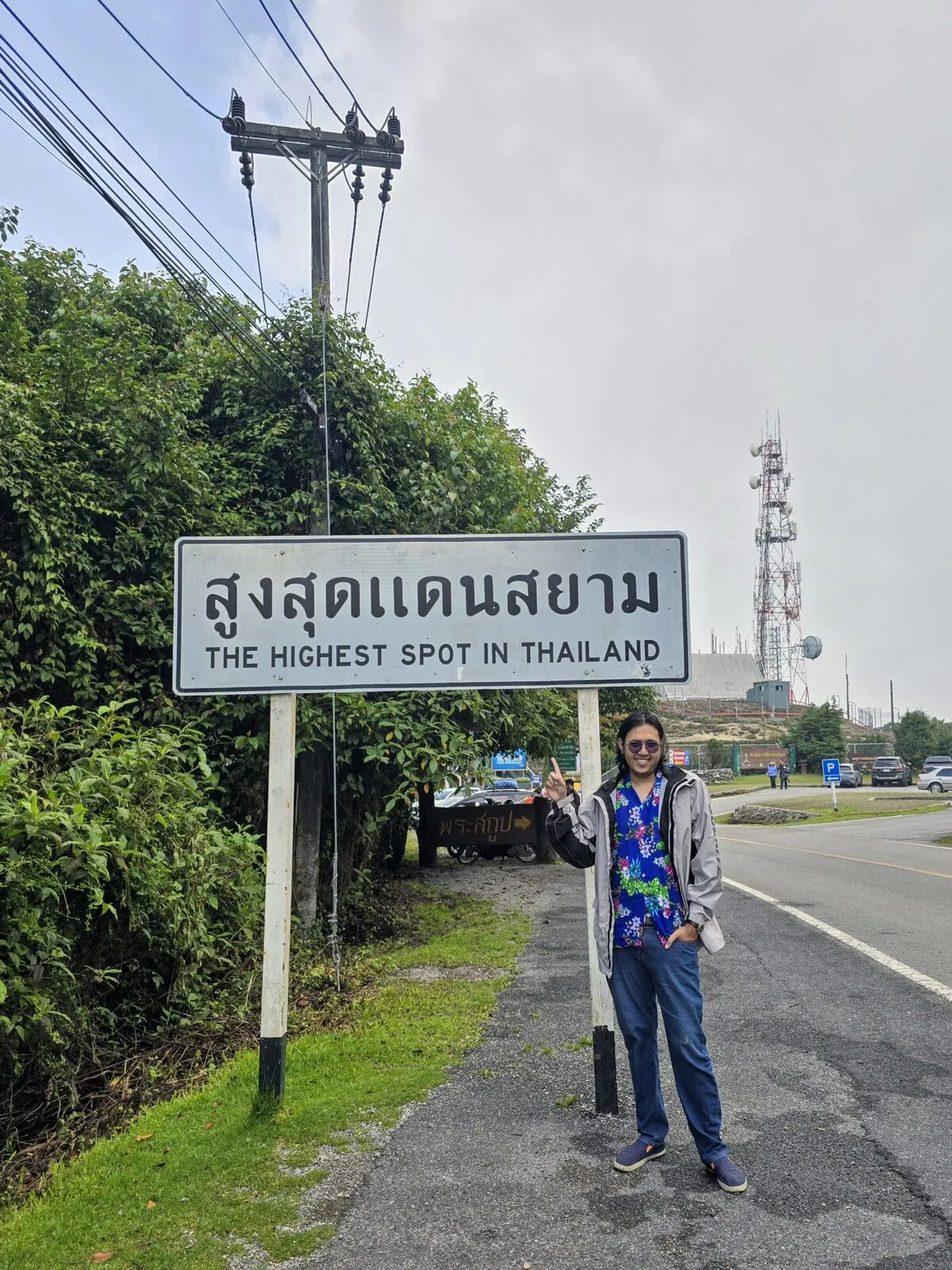 A traveller standing beside a road sign reading The Highest Spot in Thailand