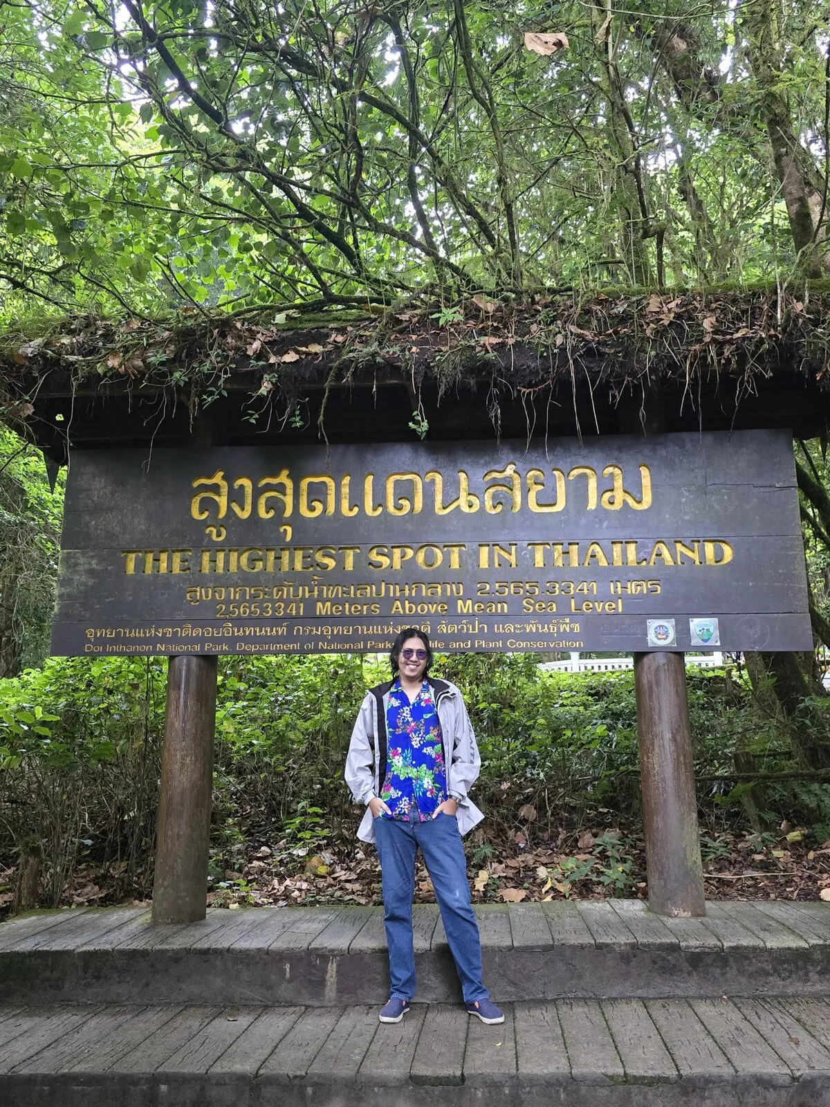 A traveller standing beneath a wooden sign reading The Highest Spot in Thailand