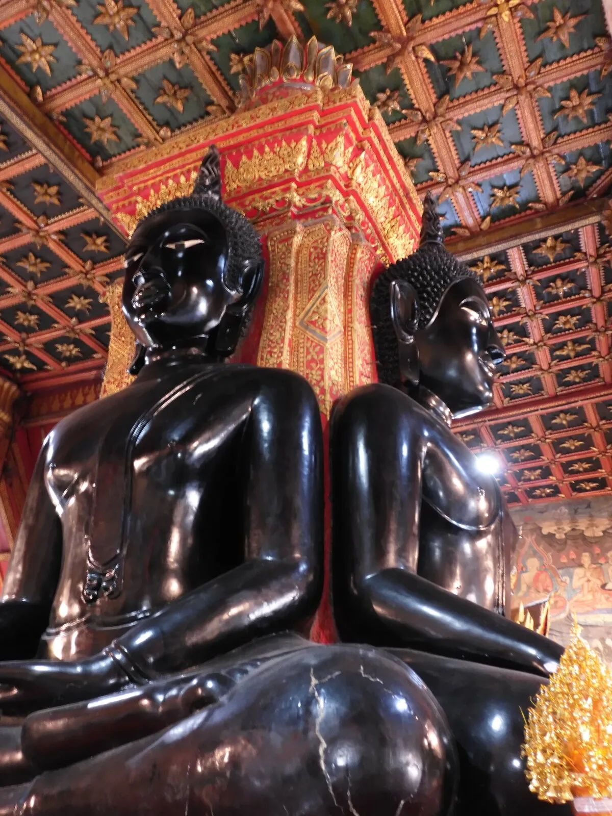 Two dark Buddha statues seated in a decorated temple hall