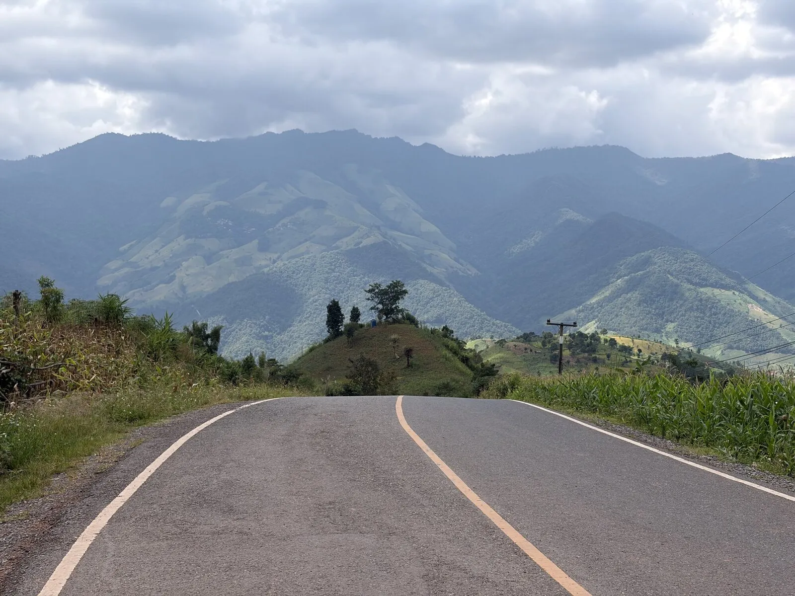An empty asphalt road leading toward layered forested mountains
