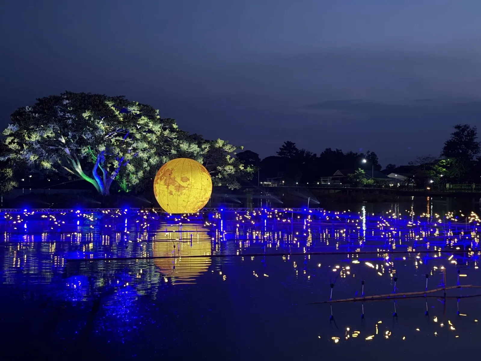 A temple courtyard at night filled with blue and gold lights reflected in water
