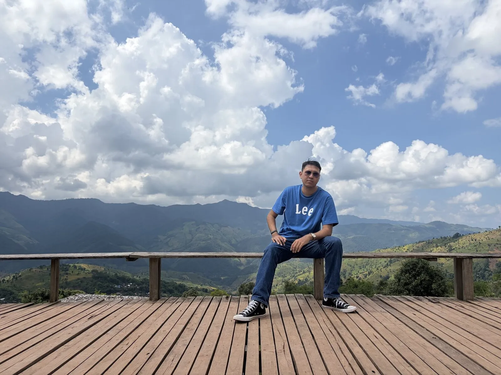 A man sitting on a wooden viewpoint deck above a mountain valley