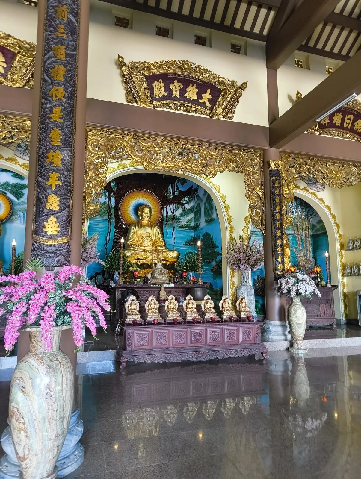 A gilded Buddha statue surrounded by flowers inside a temple hall