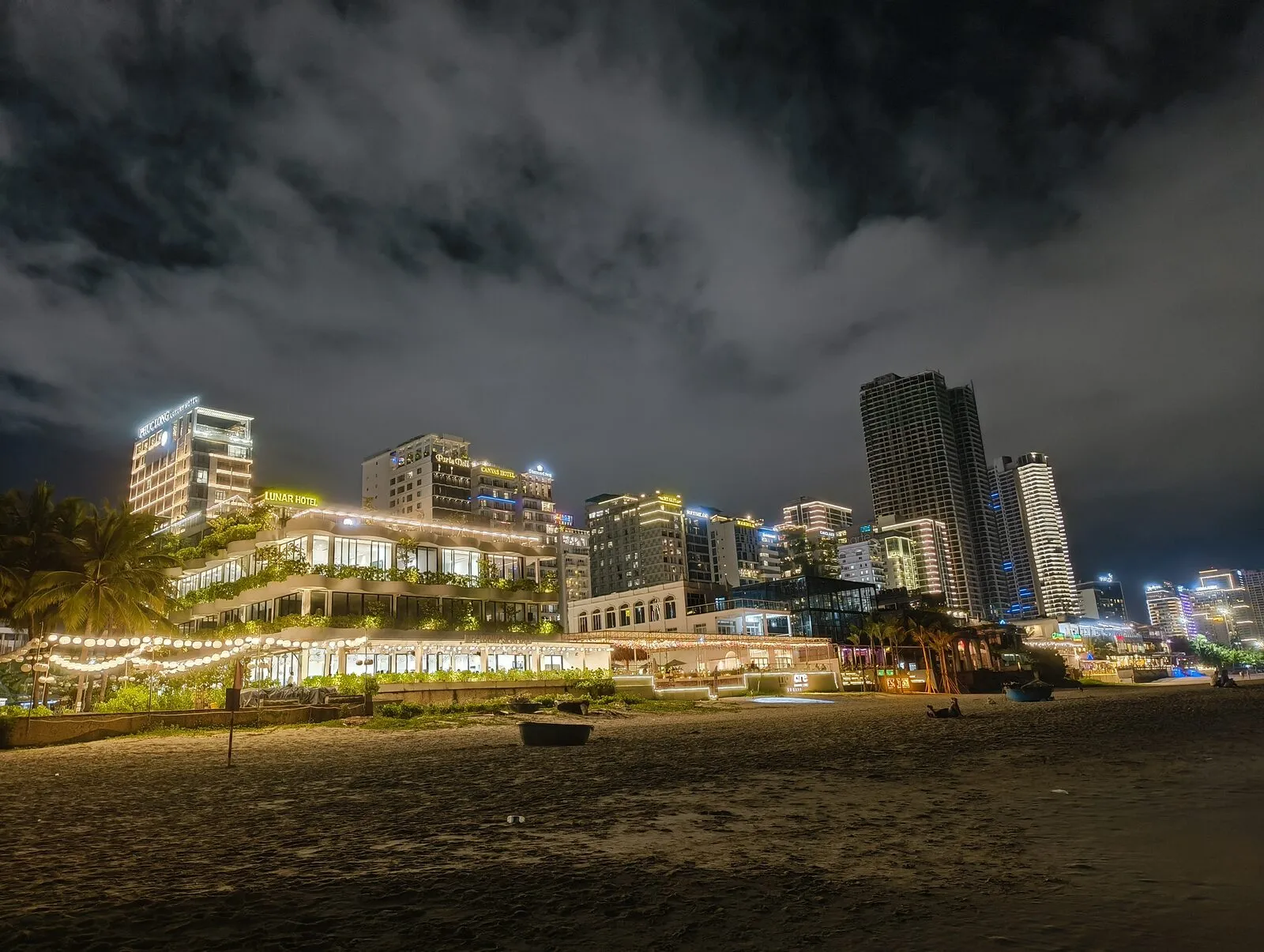 A beach at night with the lights of Da Nang behind it